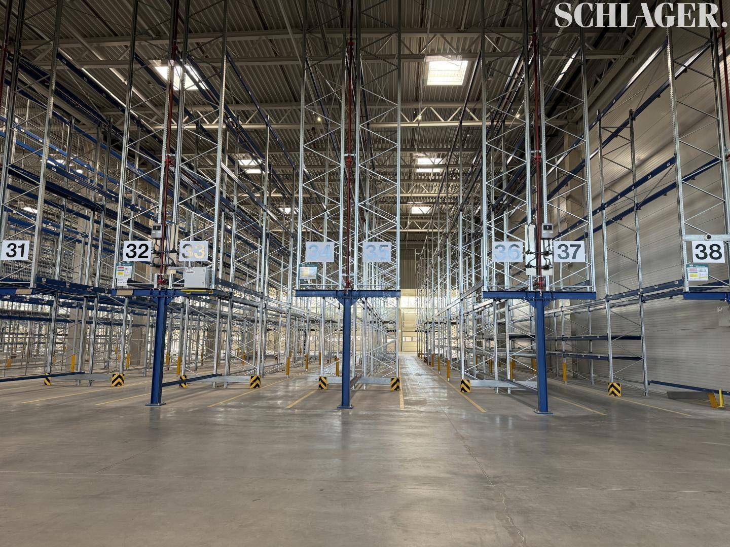 Zentraler Blick in eine Lagerhalle mit hohen Regalsystemen, Betonboden und industrieller Beleuchtung.