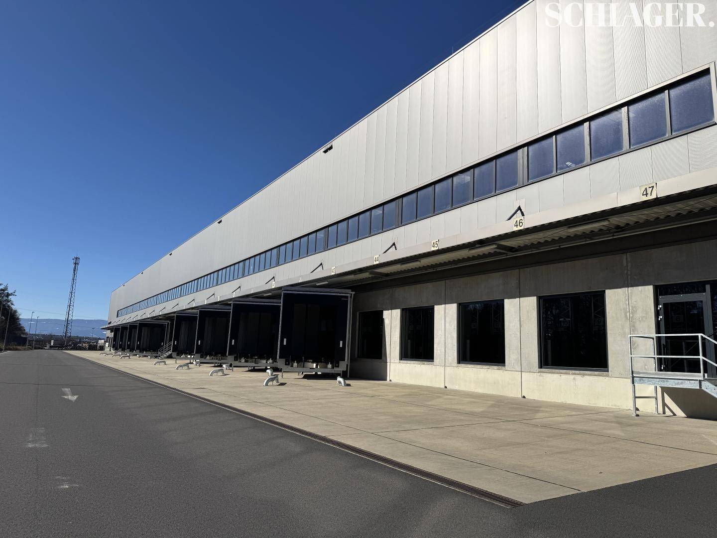 Lange Ansicht einer modernen Lagerhalle mit zahlreichen Laderampen und großen Fenstern.