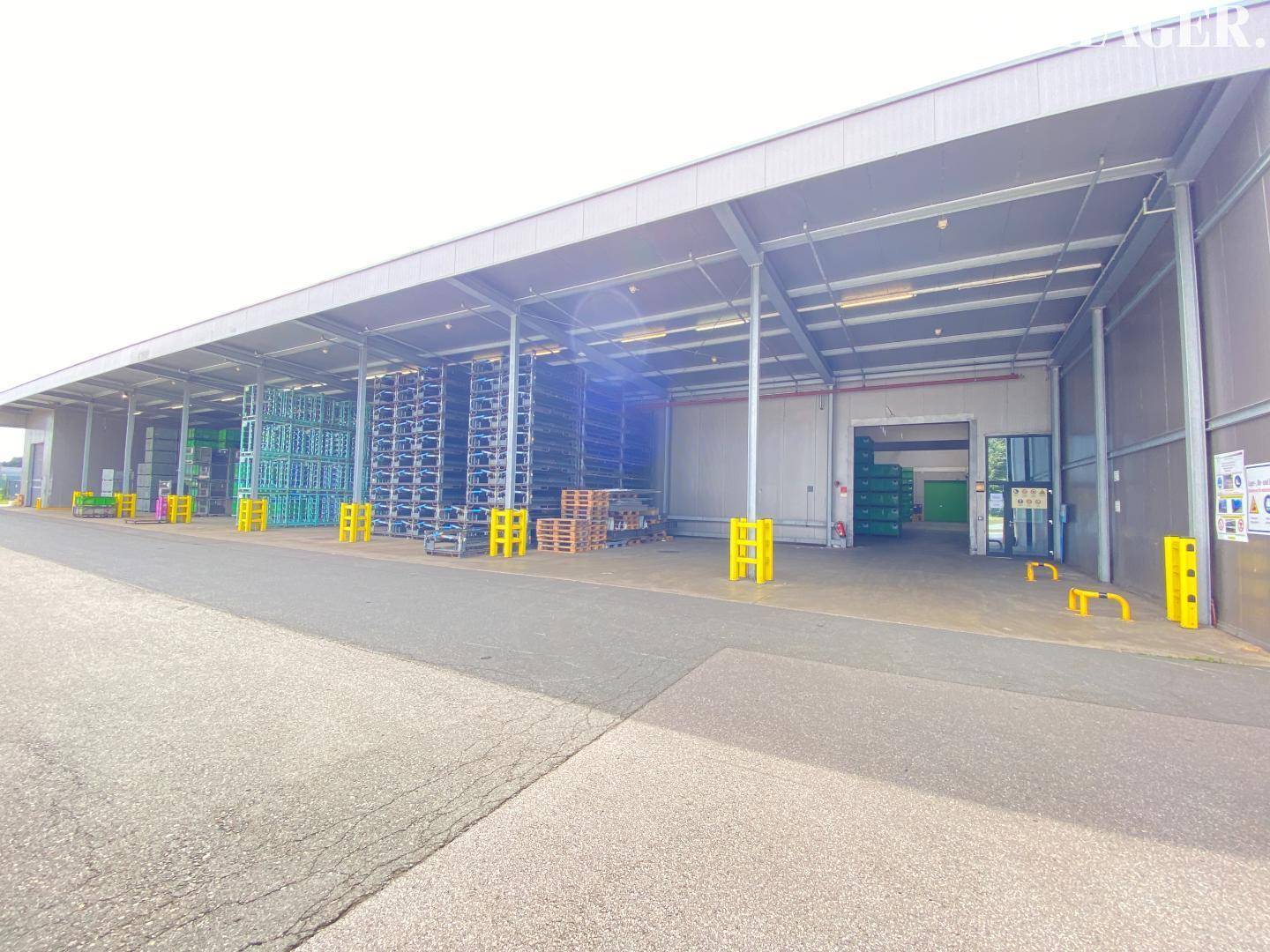Weiterer Blick auf den überdachten Ladebereich eines modernen Lagergebäudes mit Zugangstüren und gestapelten Regalen.