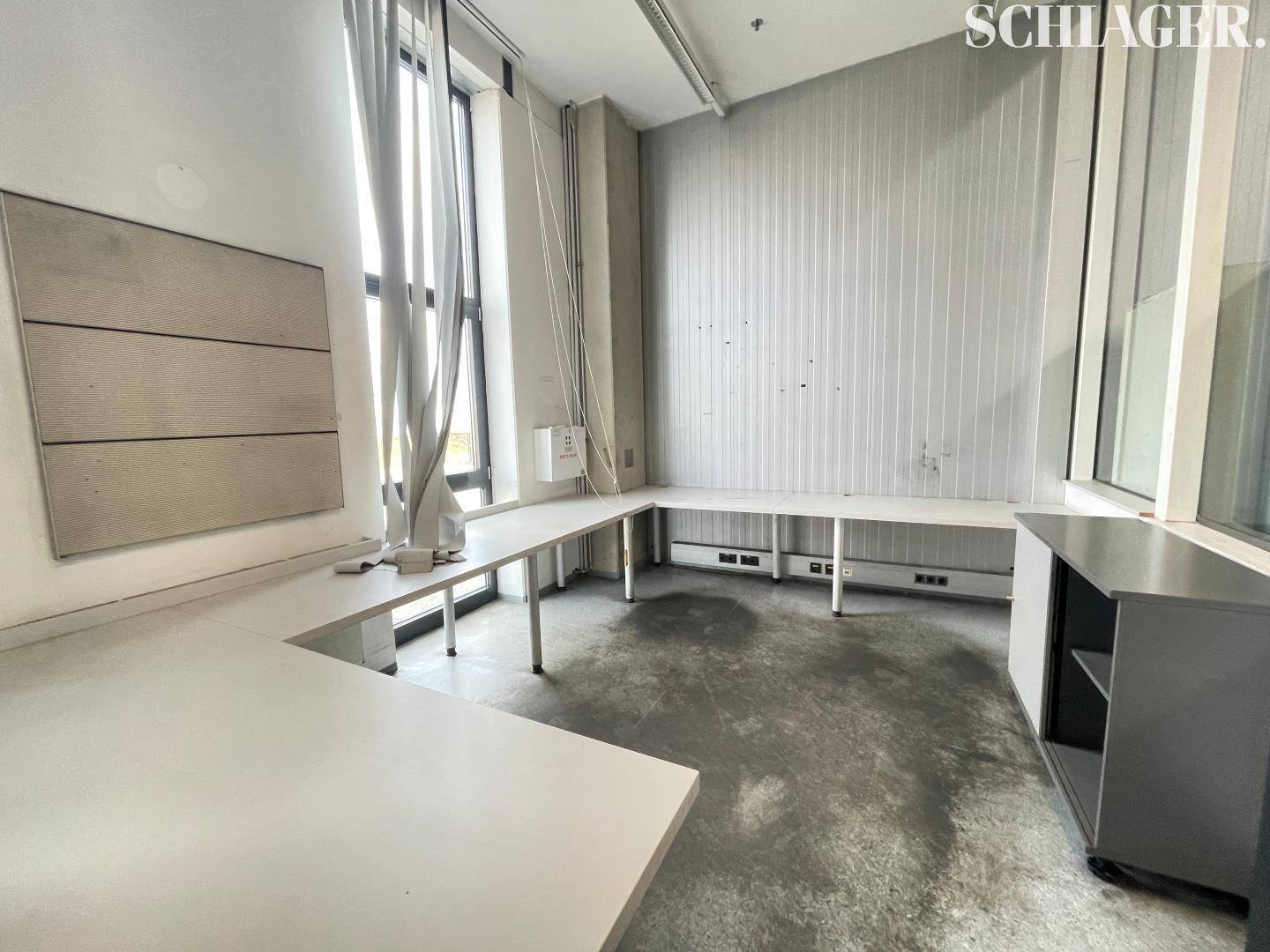 Helles Büro mit großen Fenstern, Schreibtischen und einem Betonboden in einem modernen Industriegebäude.