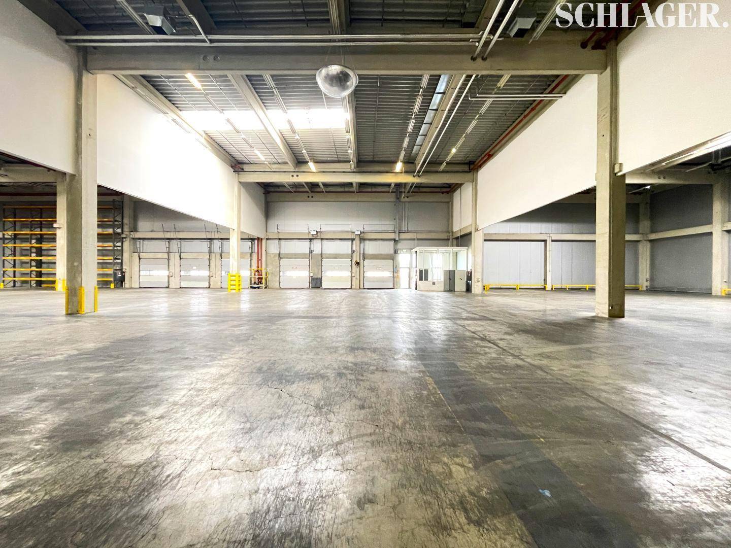 Große Lagerhalle mit mehreren Rolltoren und Betonboden, ideal für Logistik und Warenannahme.