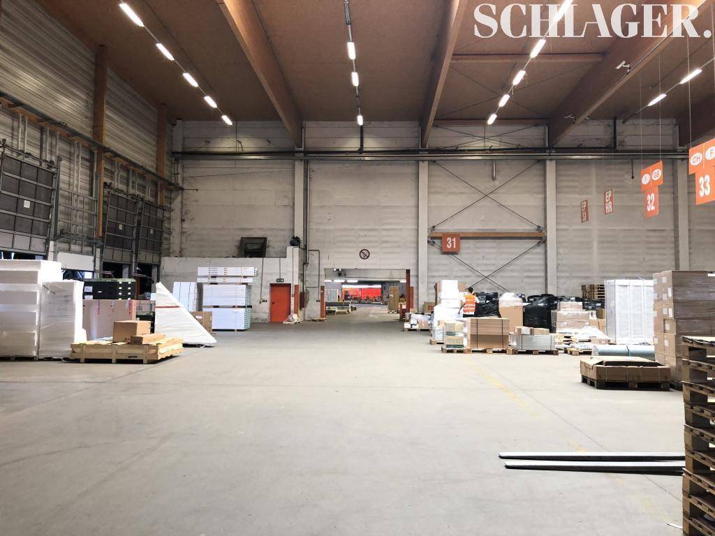 Weitläufige Lagerfläche mit hohen Wänden, Betonboden und Zugang zu weiteren Hallenbereichen.