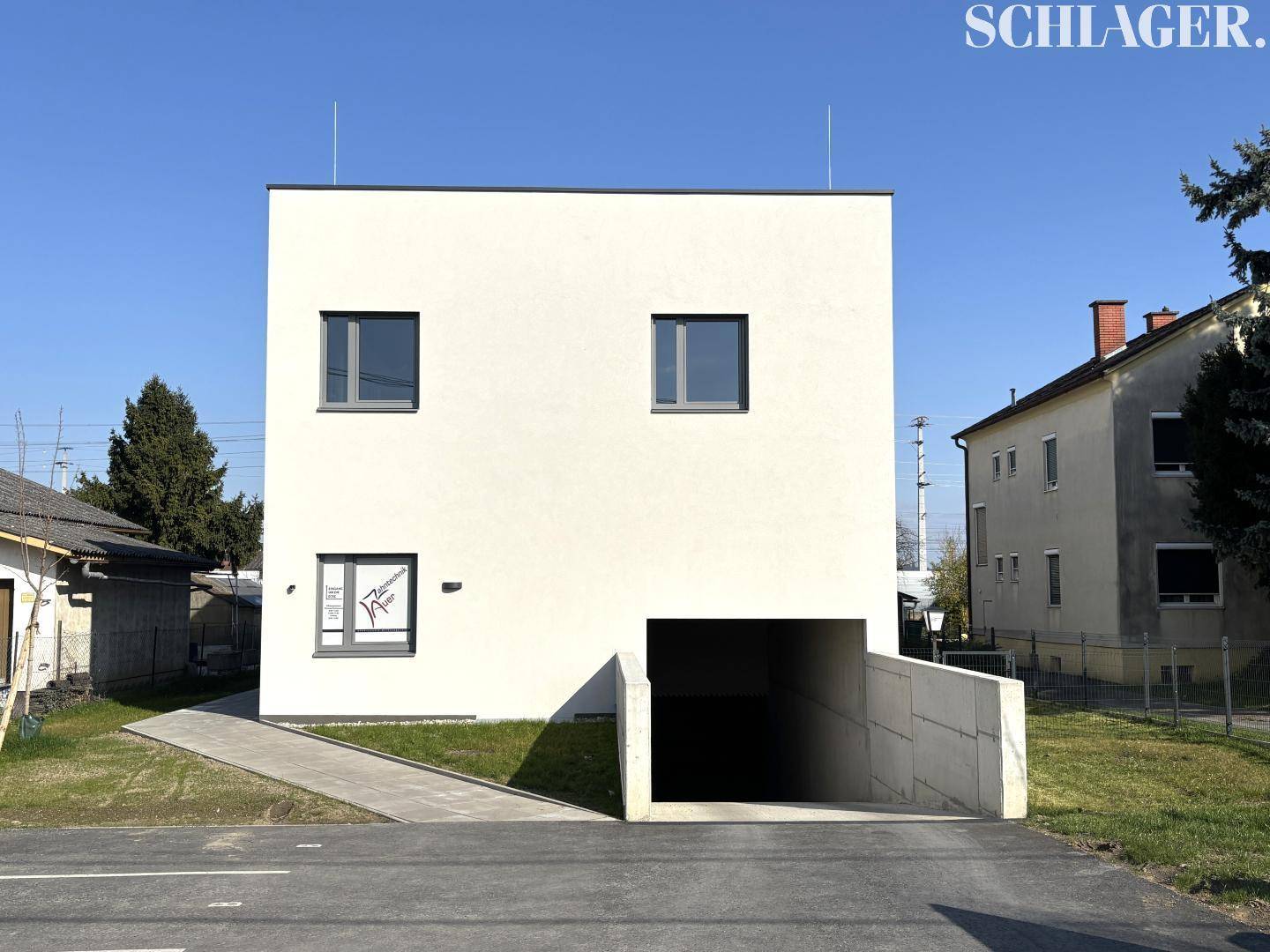 Modernes, weißes Gebäude mit minimalistischer Fassade und integrierter Tiefgarageneinfahrt.