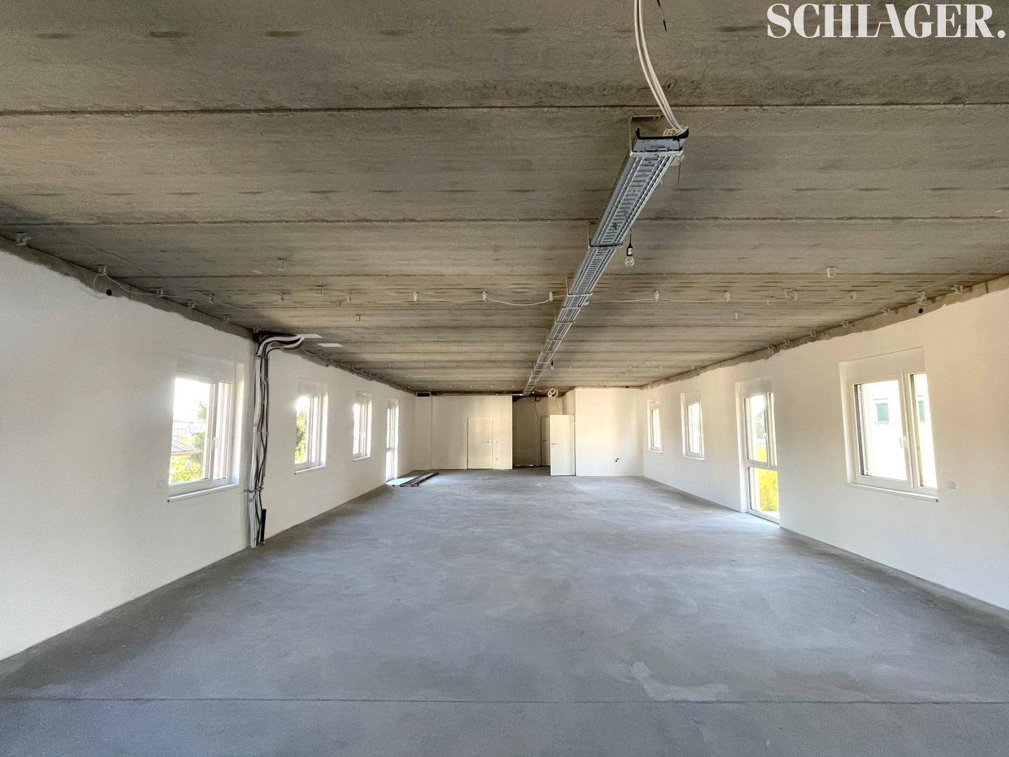 Großer, leerer Raum mit Betonboden und vielen Fenstern, bereit für den Innenausbau.