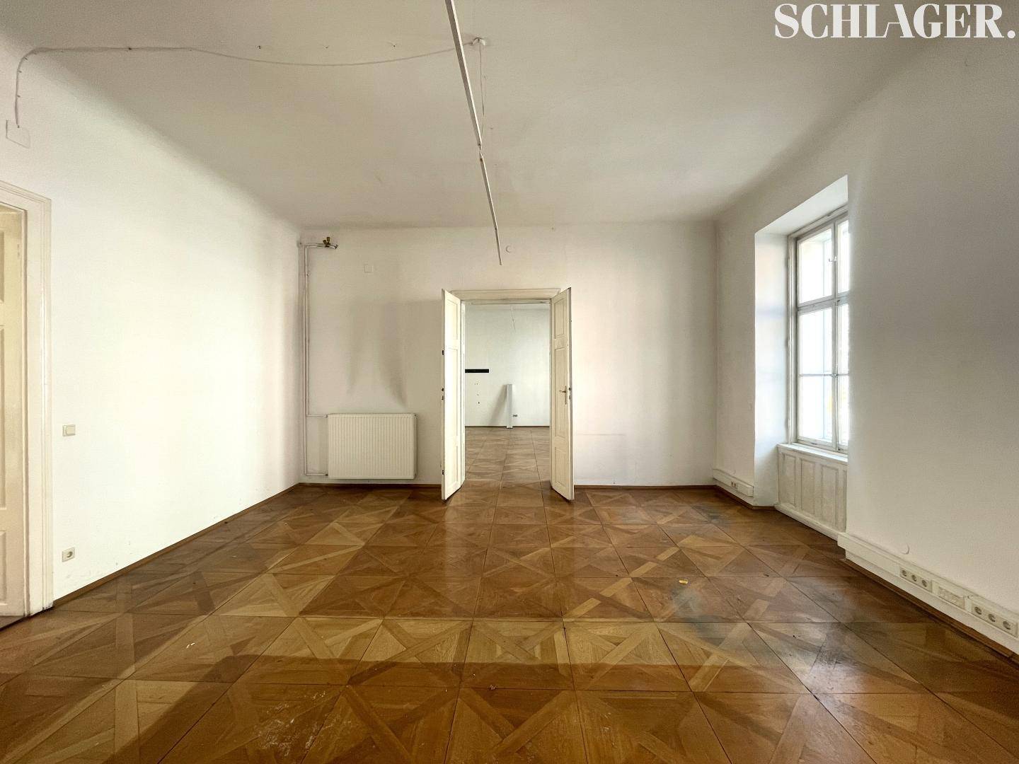 Heller Raum mit Holzboden und zwei Türen, die zu angrenzenden Zimmern führen.