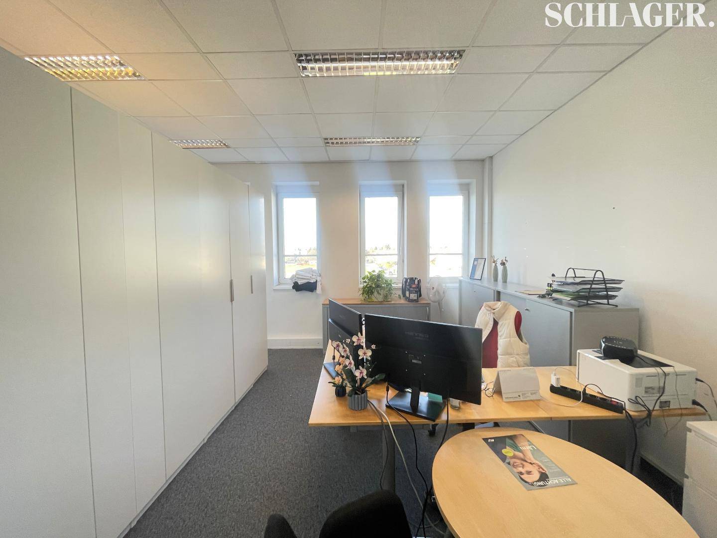Helles Büro mit integrierten weißen Schränken, zwei Arbeitsplätzen und Fenstern für viel Tageslicht.