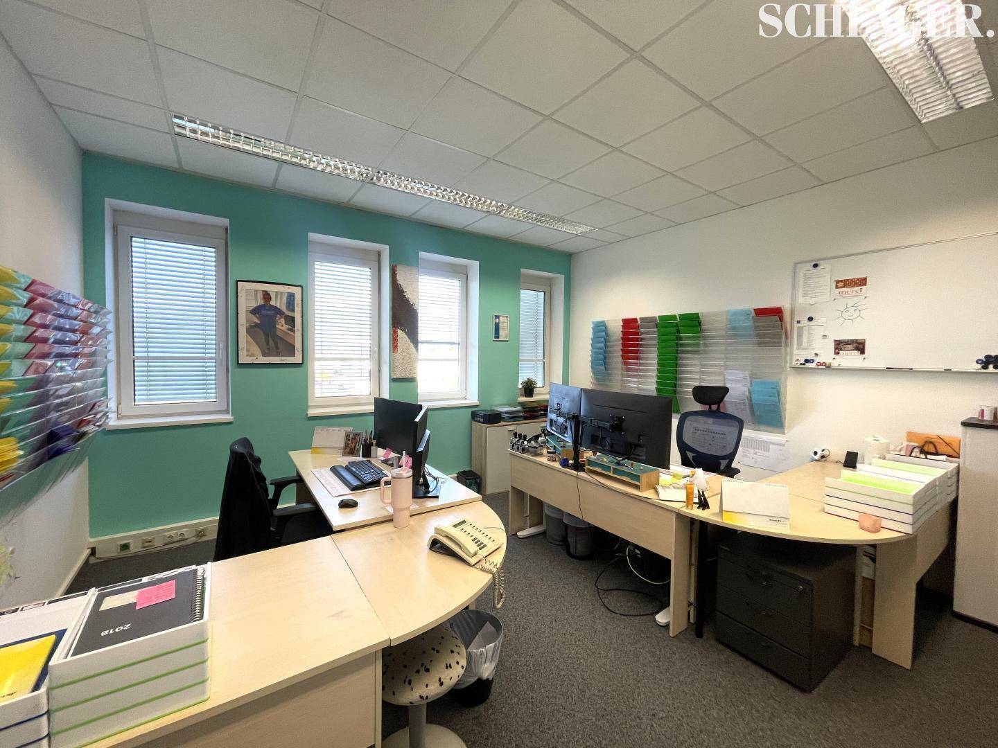 Geräumiges Büro mit mehreren Arbeitsplätzen, modernen Schreibtischen und Fenstern mit Jalousien.
