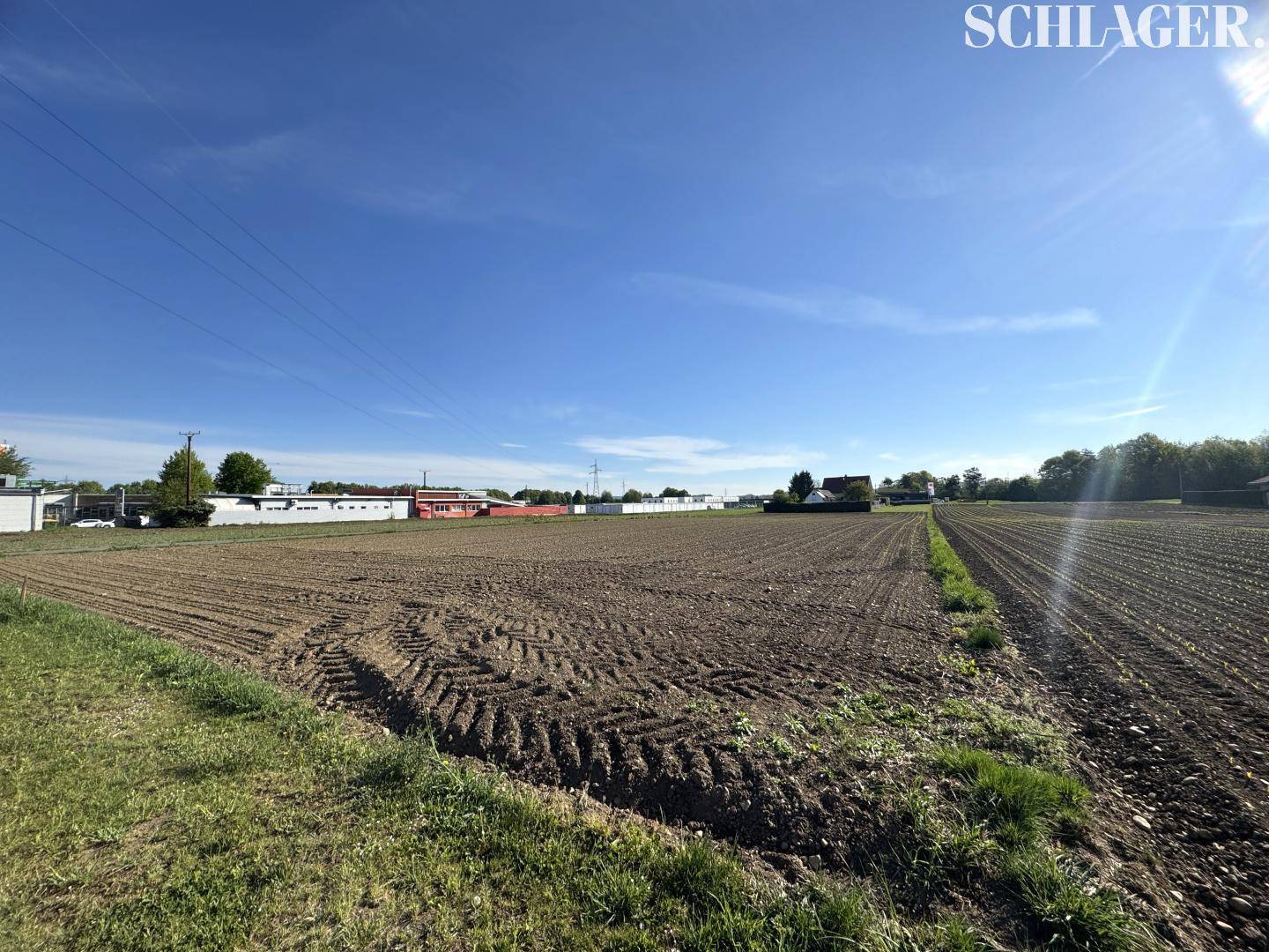 Weitläufiges Ackerland unter strahlend blauem Himmel mit vereinzelter Bebauung in der Ferne.
