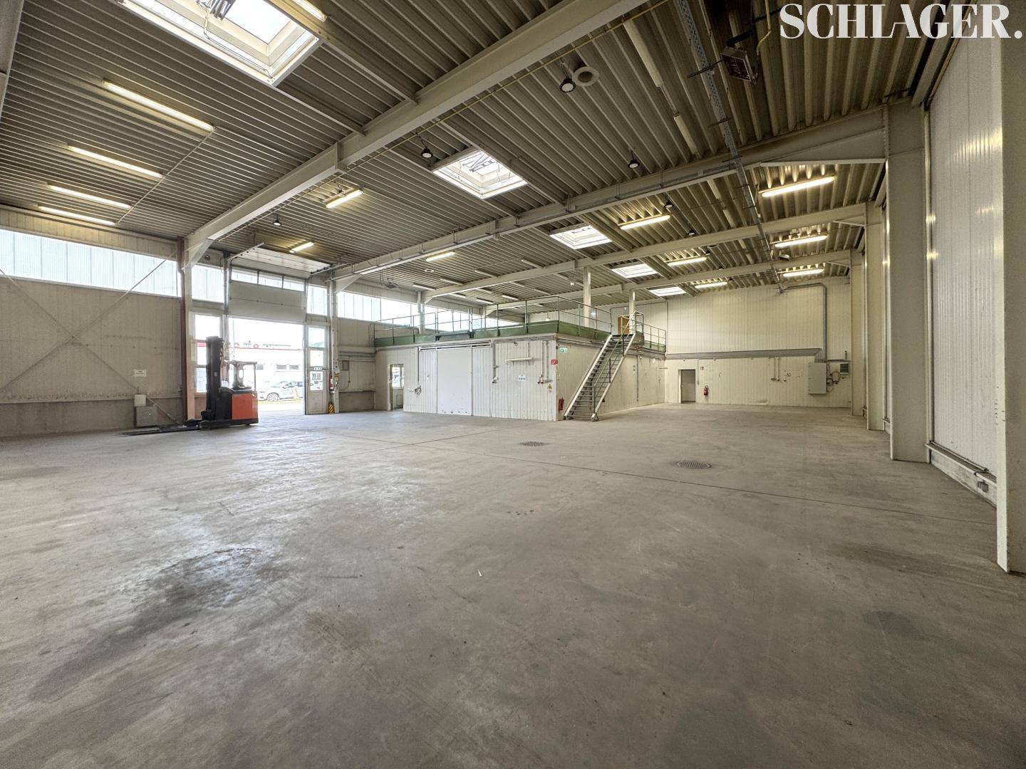 Weitläufige Lagerhalle mit Betonboden, Oberlichtern und einer erhöhten Plattform mit Treppe.