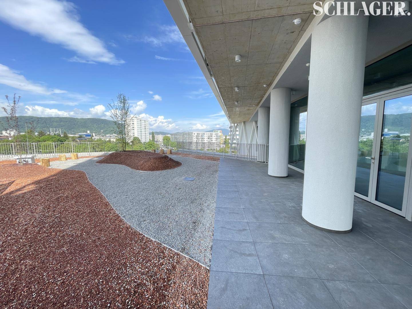 Begrünte Dachterrasse mit Kiesflächen, Rindenmulch und Säulen, die einen entspannenden Außenbereich schaffen.