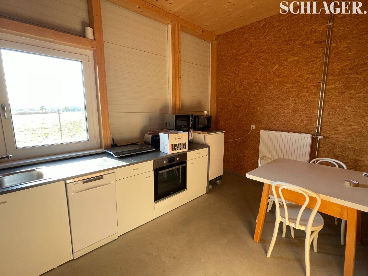 Kleine Küche mit weißen Einbauschränken, Spüle, Backofen und einem Esstisch mit Stühlen.