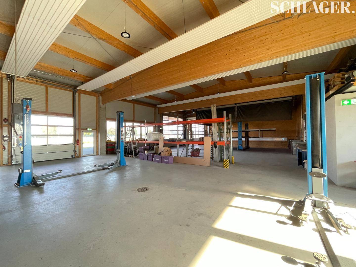 Geräumige Werkstatthalle mit Hebebühnen, hohen Decken und sichtbaren Holzträgern, gut beleuchtet.