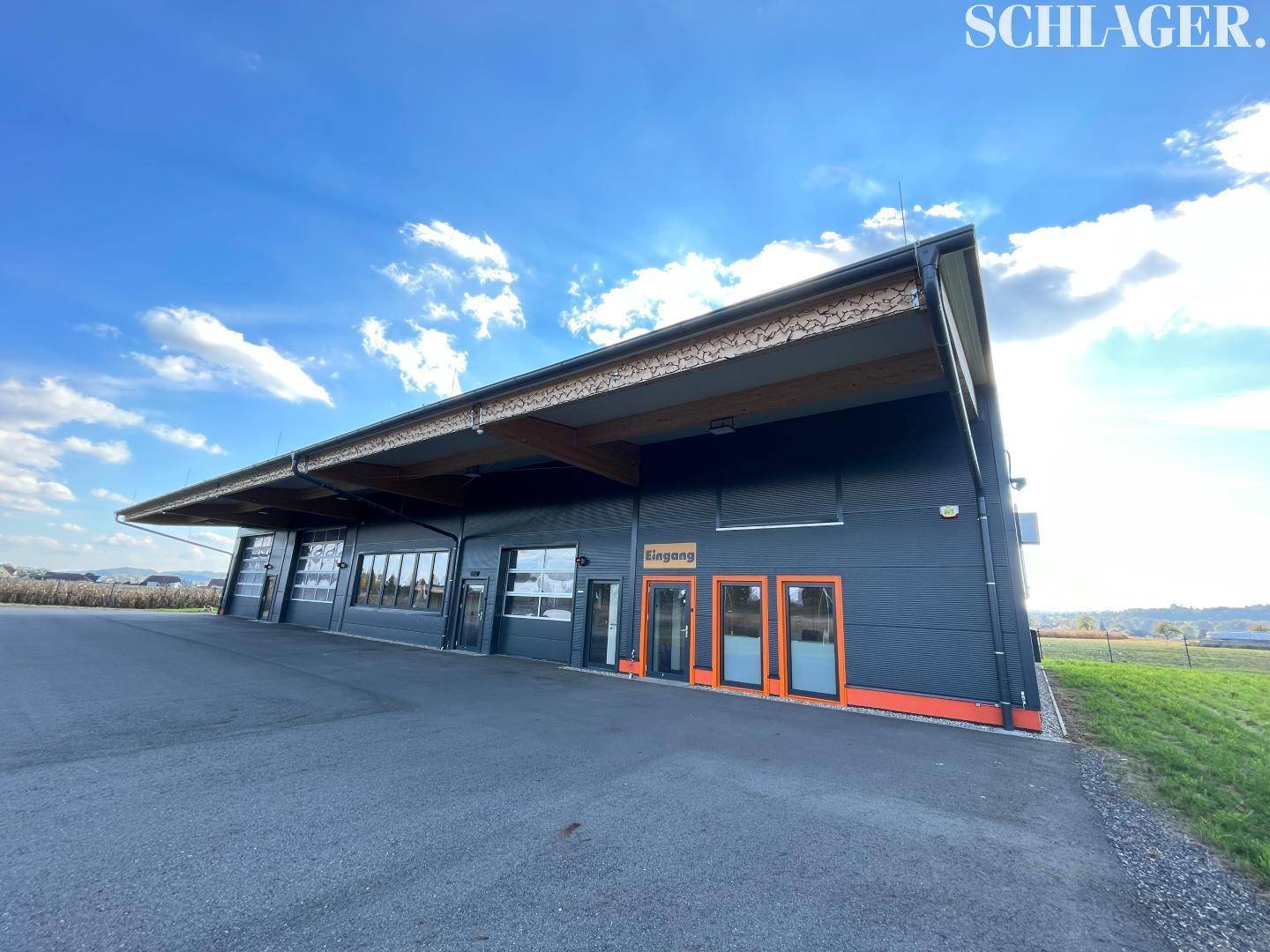 Außenansicht des modernen Gewerbegebäudes mit markantem Eingangsbereich, großen Rolltoren und Holzbalken.