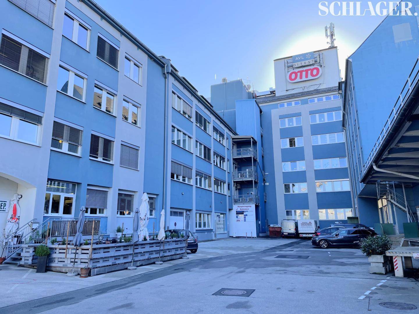 Hinterhofansicht des Bürokomplexes mit Ladezonen und geparkten Fahrzeugen unter blauem Himmel.