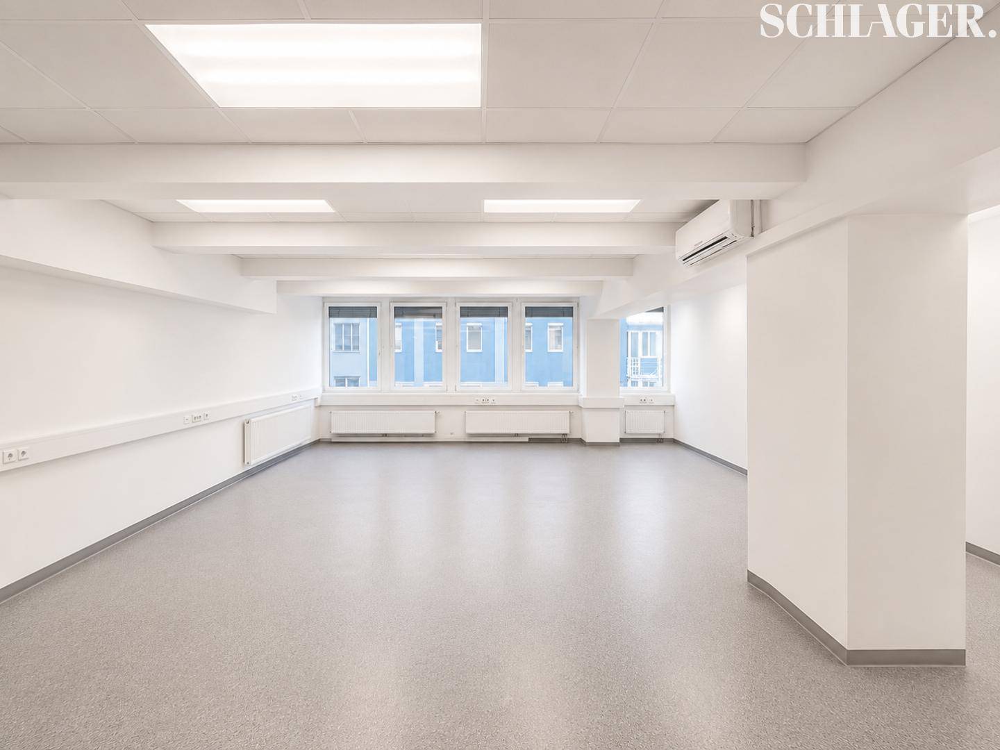 Heller, leerer Büroraum mit großen Fenstern, Klimaanlage und grauem Vinylboden.