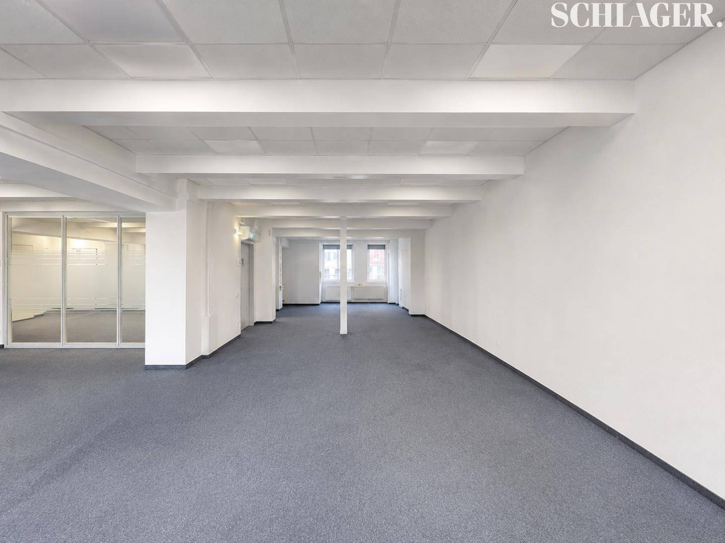 Geräumiger, unmöblierter Bürobereich mit grauem Teppichboden und abgehängter Decke.