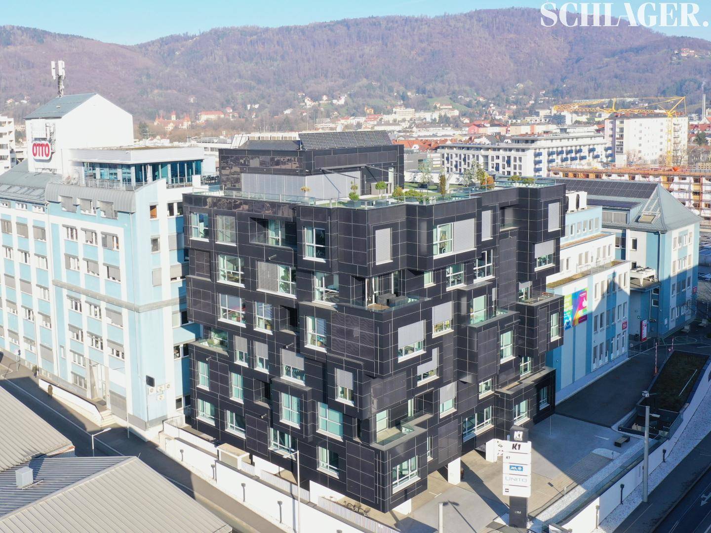 Luftaufnahme des modernen Bürogebäudes mit Dachterrasse und Blick auf die Stadt und die umliegenden Berge.