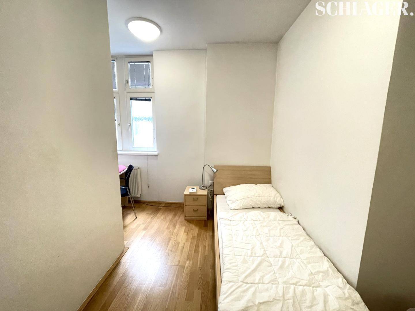 Kleines Schlafzimmer mit Einzelbett, Nachttisch und Fenster, das Tageslicht hereinlässt.