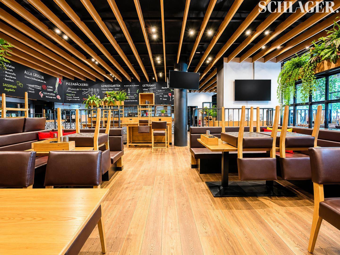 Gemütlicher Restaurantbereich mit Holzbalkendecke, braunen Sitzbänken und Tischen, bereit für Gäste.