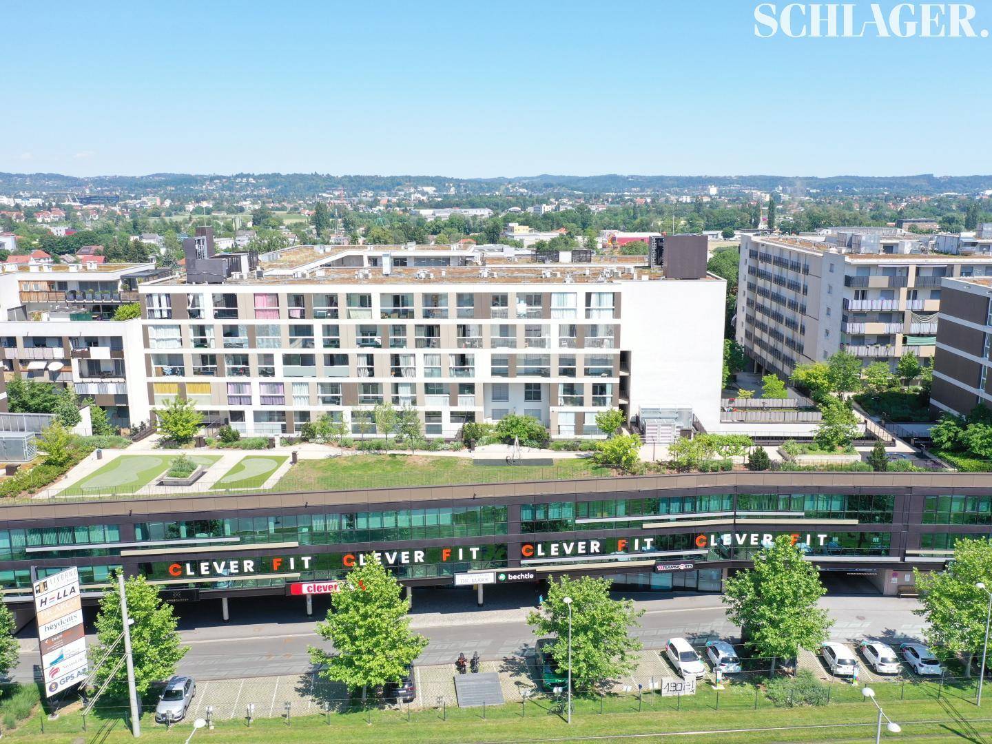 Luftaufnahme eines modernen Gebäudekomplexes mit Geschäften im Erdgeschoss und Wohnungen darüber.
