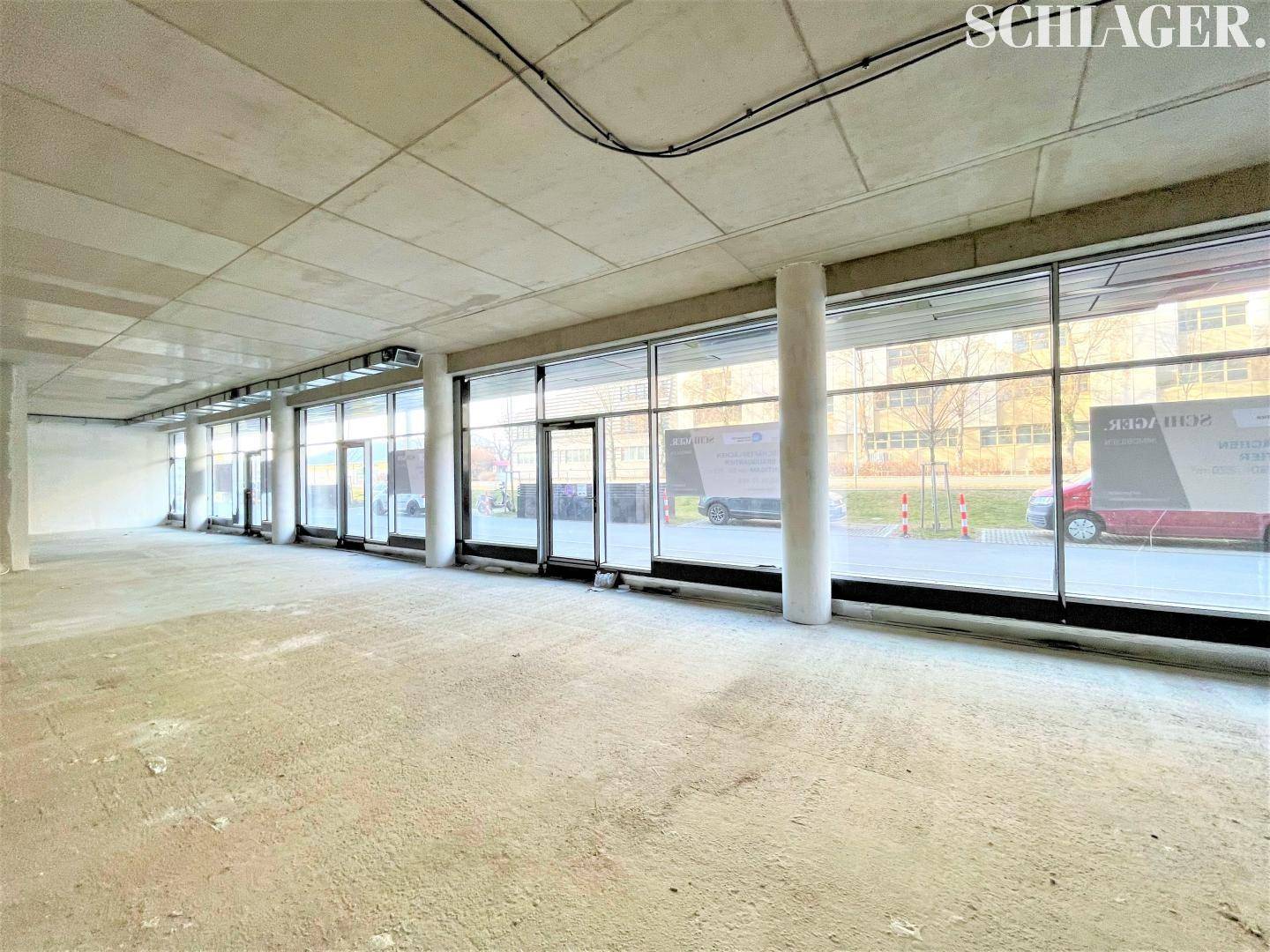Großer, leerer Gewerberaum mit Betonboden und raumhohen Fenstern, bereit für den Ausbau.