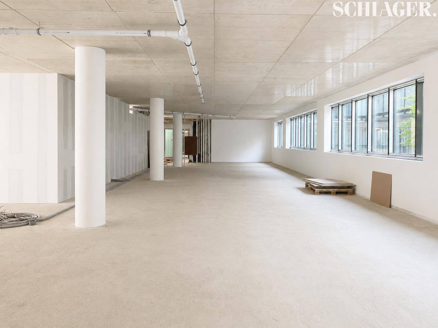 Großer, leerer Gewerberaum mit hohen Decken, Betonboden und großen Fenstern, bereit für den Ausbau.