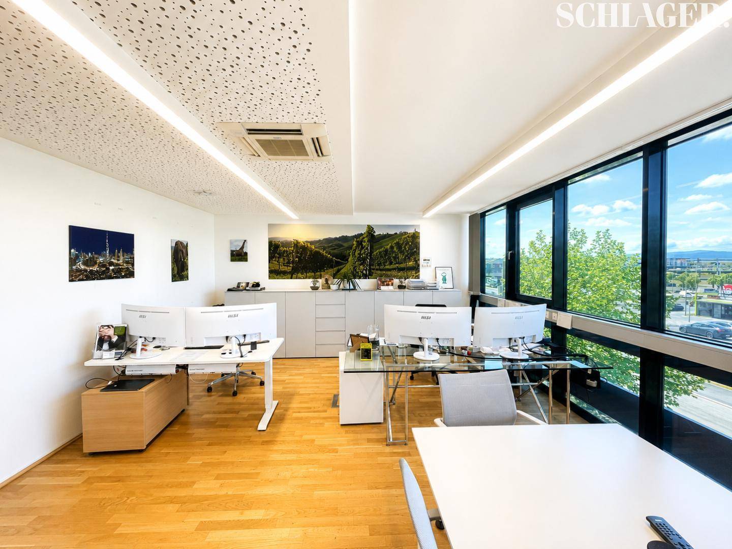 Modernes Büro mit mehreren Arbeitsplätzen, großen Fenstern und Blick auf die Umgebung.