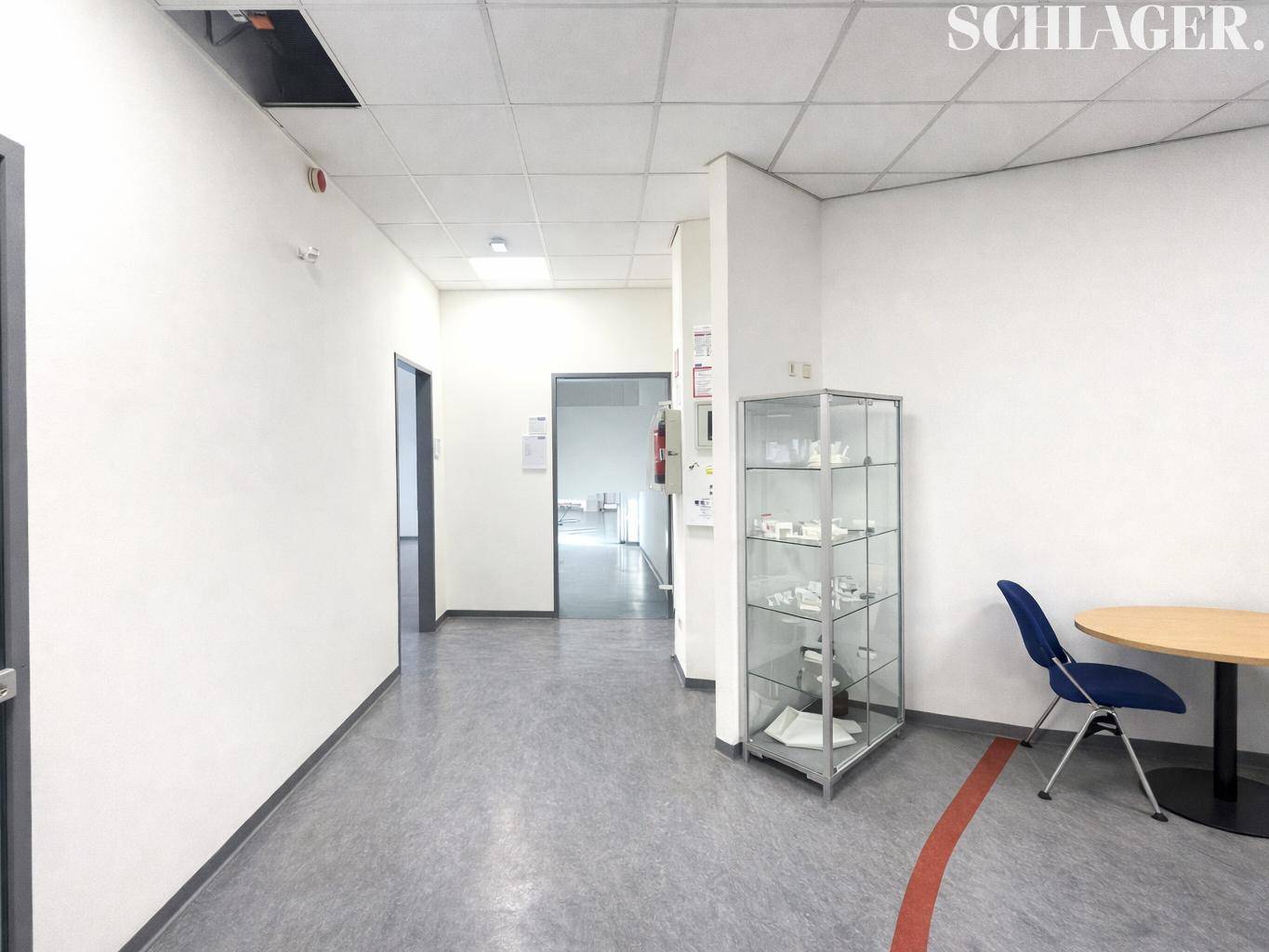 Heller Flur mit Vinylboden, einer Vitrine und einem kleinen Tisch mit Stuhl.