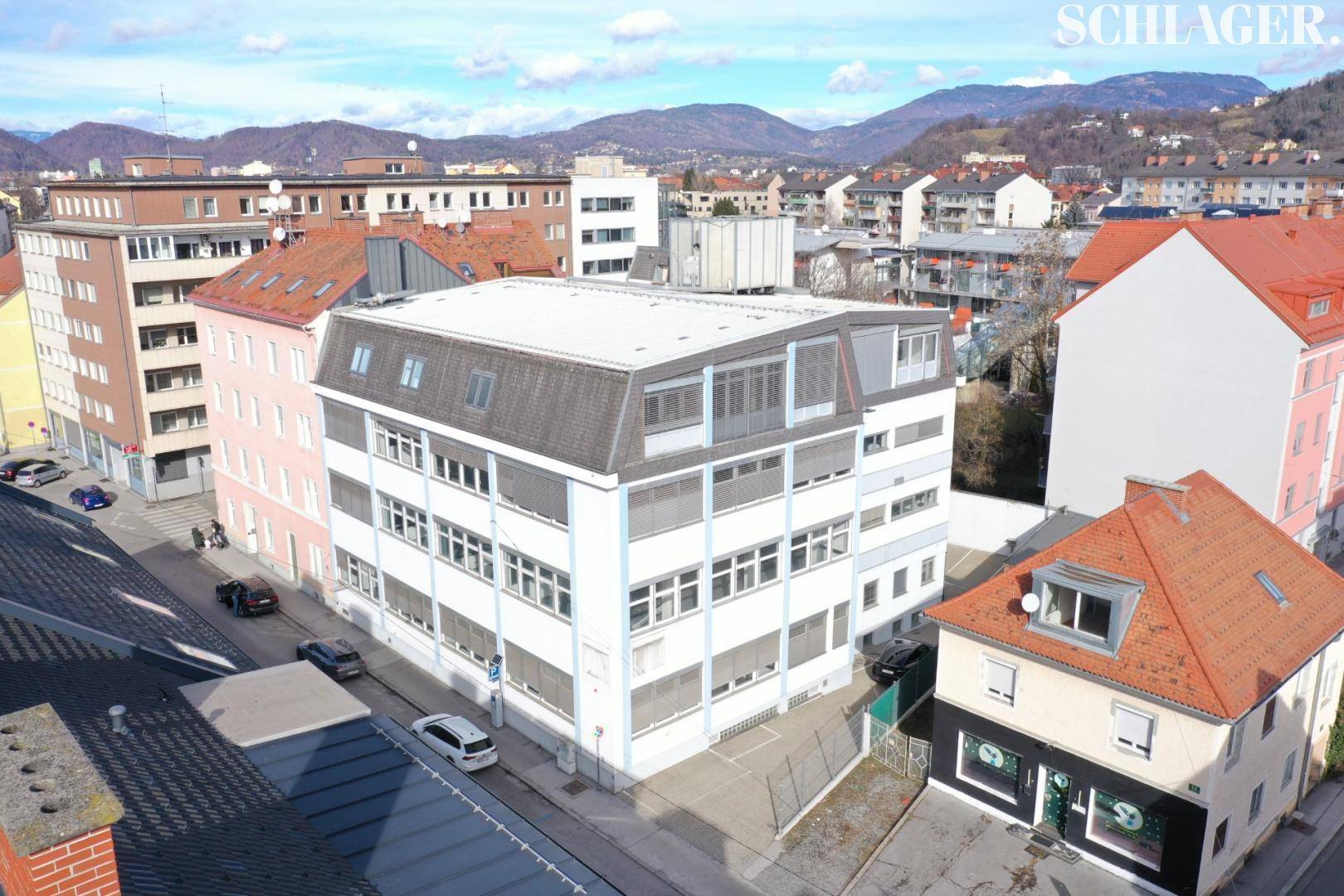 Luftaufnahme des Bürogebäudes in städtischer Umgebung mit Bergen im Hintergrund.