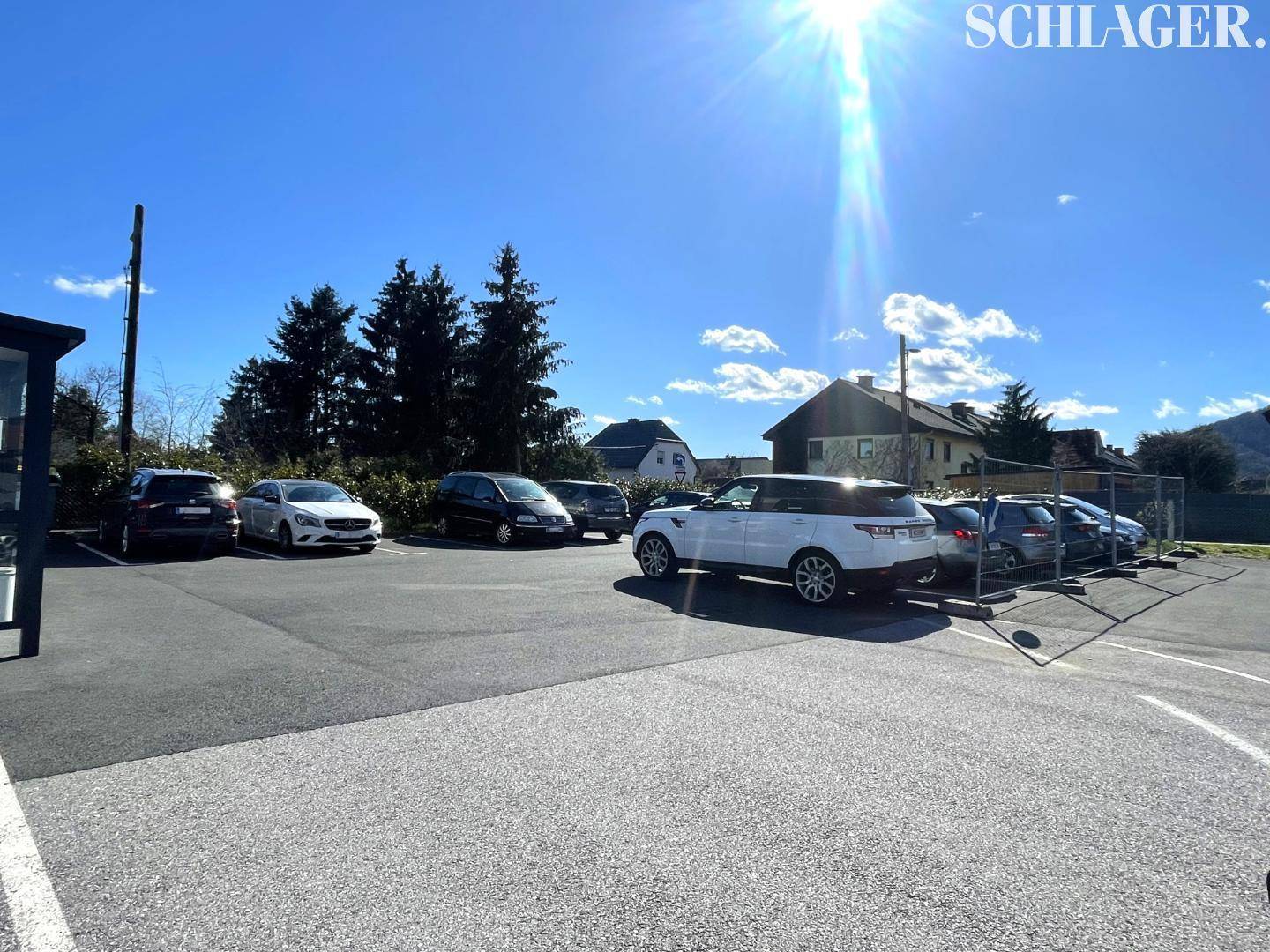 Großer Außenparkplatz mit mehreren Autos unter strahlendem Sonnenschein und blauem Himmel.