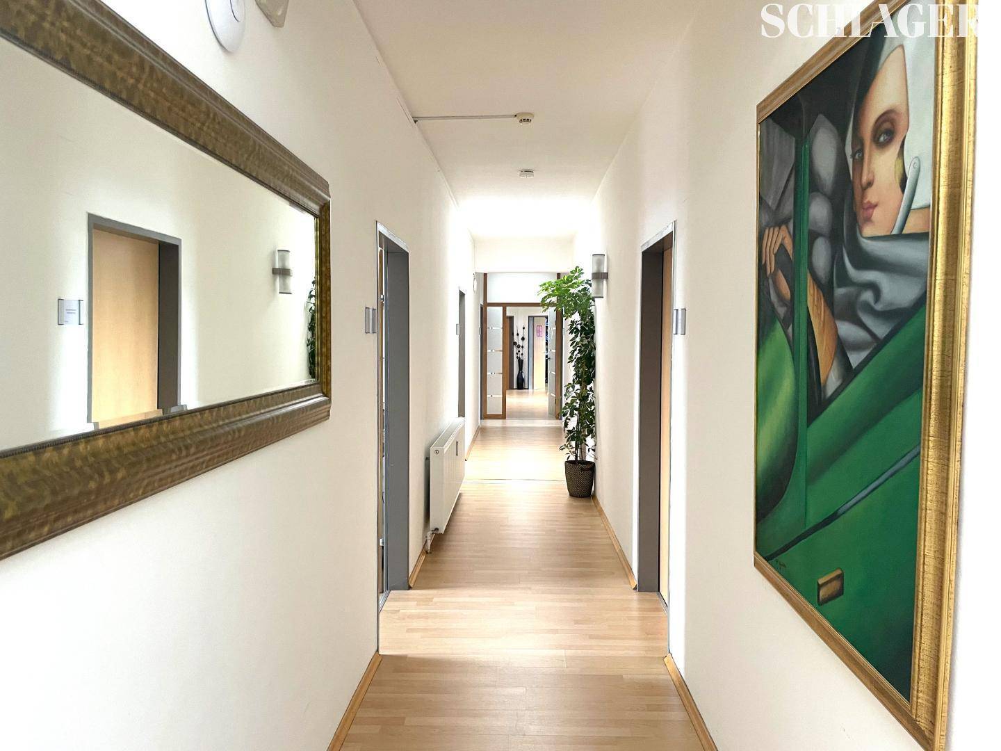 Langer Flur mit Holzboden, Spiegel, Kunstwerken und Türen, der zu weiteren Räumen führt.