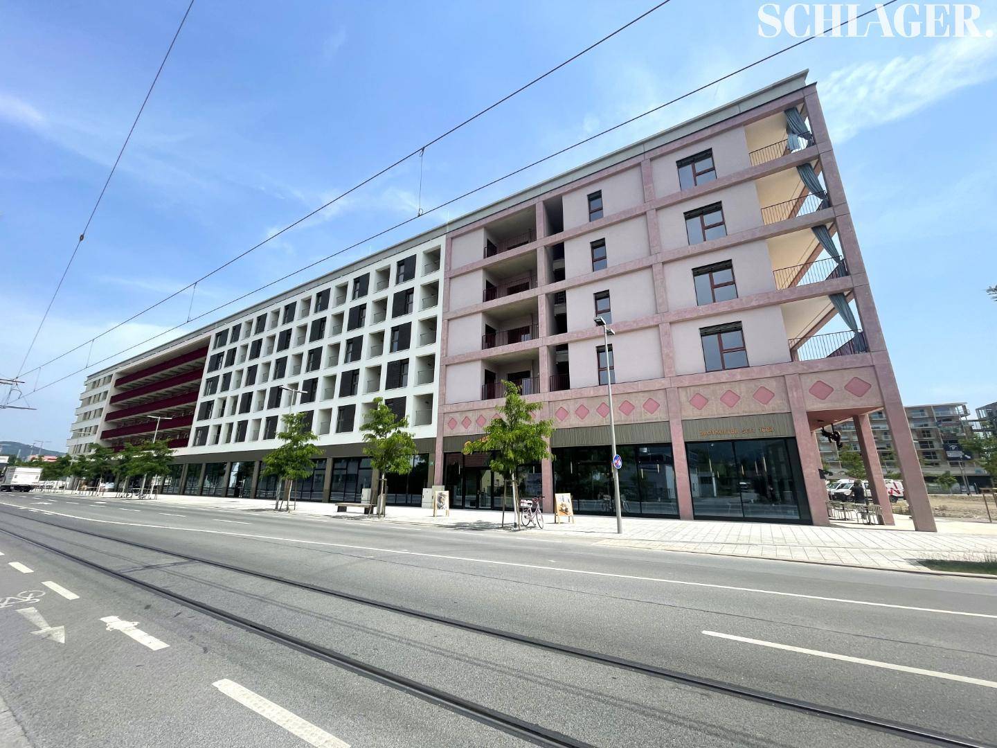 Moderne Gebäudefassade mit großen Fenstern und Balkonen, direkt an einer Straße mit Straßenbahnschienen.