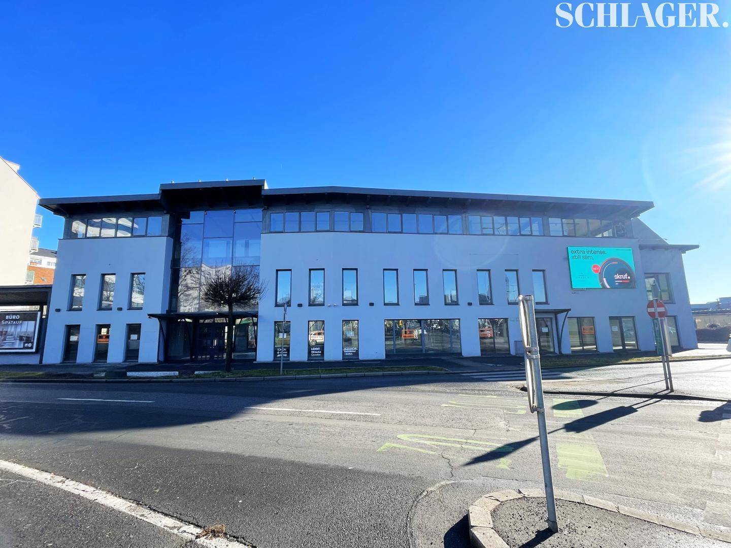 Ansicht des modernen Geschäftsgebäudes mit großer Glasfront und digitaler Werbeanzeige bei Sonnenschein.