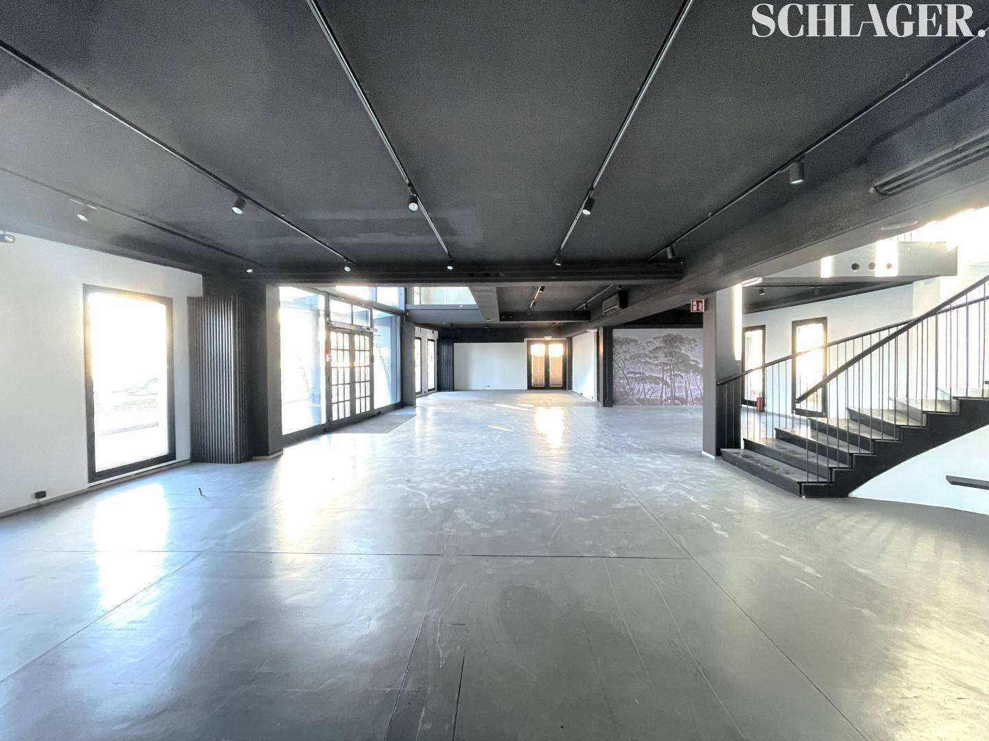 Geräumiger, offener Verkaufsraum mit Betonboden, schwarzer Decke und einer modernen Treppe.