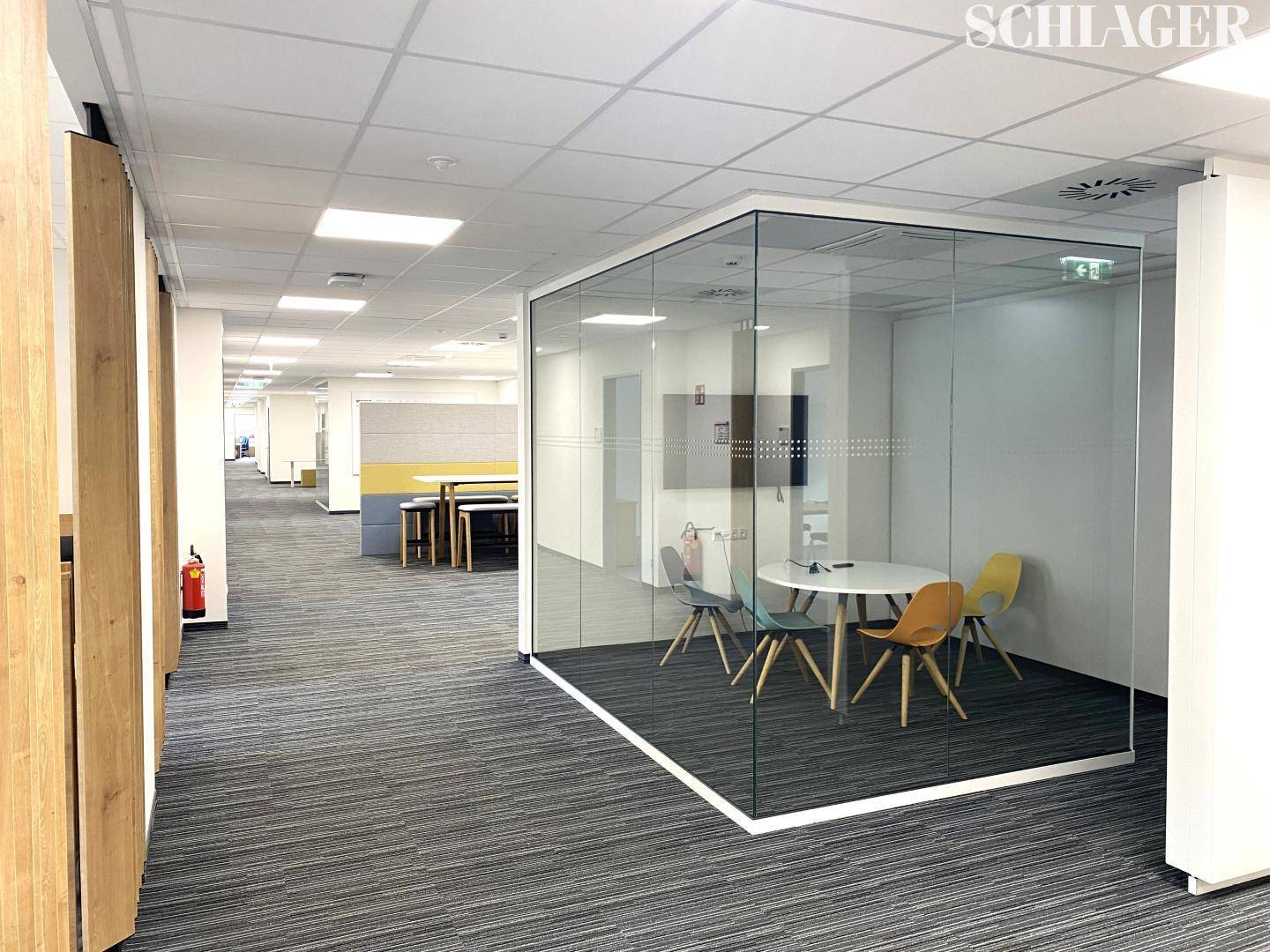 Offener Bürobereich mit Teppichboden und einem gläsernen Besprechungsraum in zeitgemäßem Design.