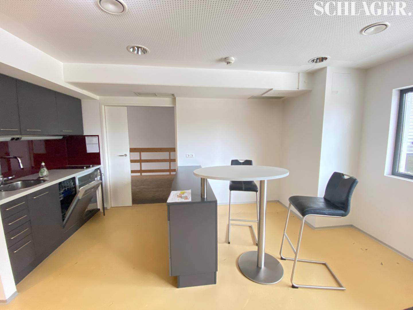 Kleine, moderne Küchenzeile mit grauen Schränken, Spülmaschine und einem Bartisch mit Hockern.