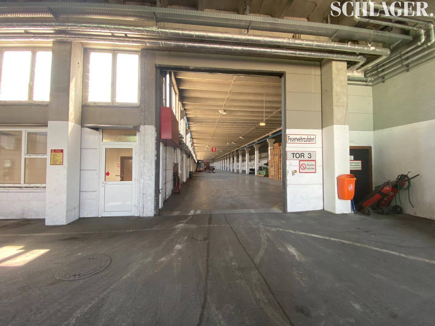 Blick durch ein großes Rolltor in eine weitläufige Industriehalle mit Betonboden und hohen Decken, ideal für Logistik.