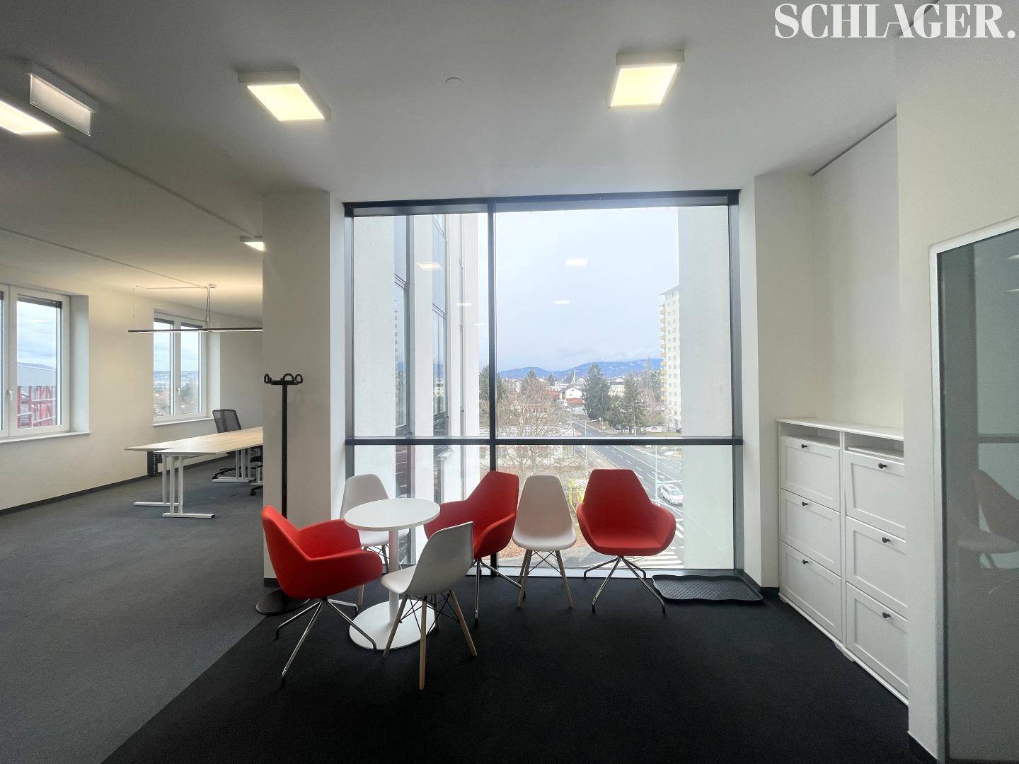 Heller Loungebereich im Büro mit farbigen Stühlen und einem großen Fenster mit Stadtblick.