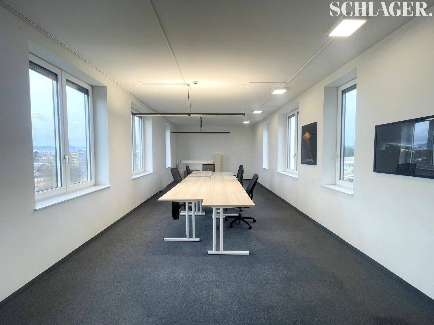 Moderner Büroraum mit langen Tischen und Stühlen, ideal für Teamarbeit oder Besprechungen.