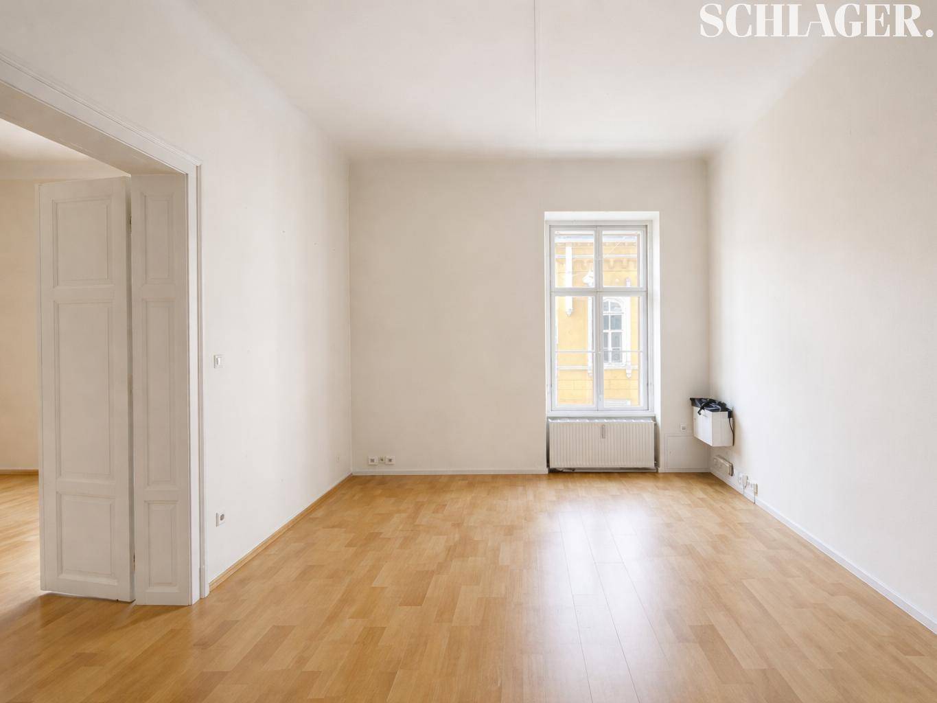 Geräumiger, heller Raum mit Holzboden und einem großen Fenster, das viel Tageslicht hereinlässt.