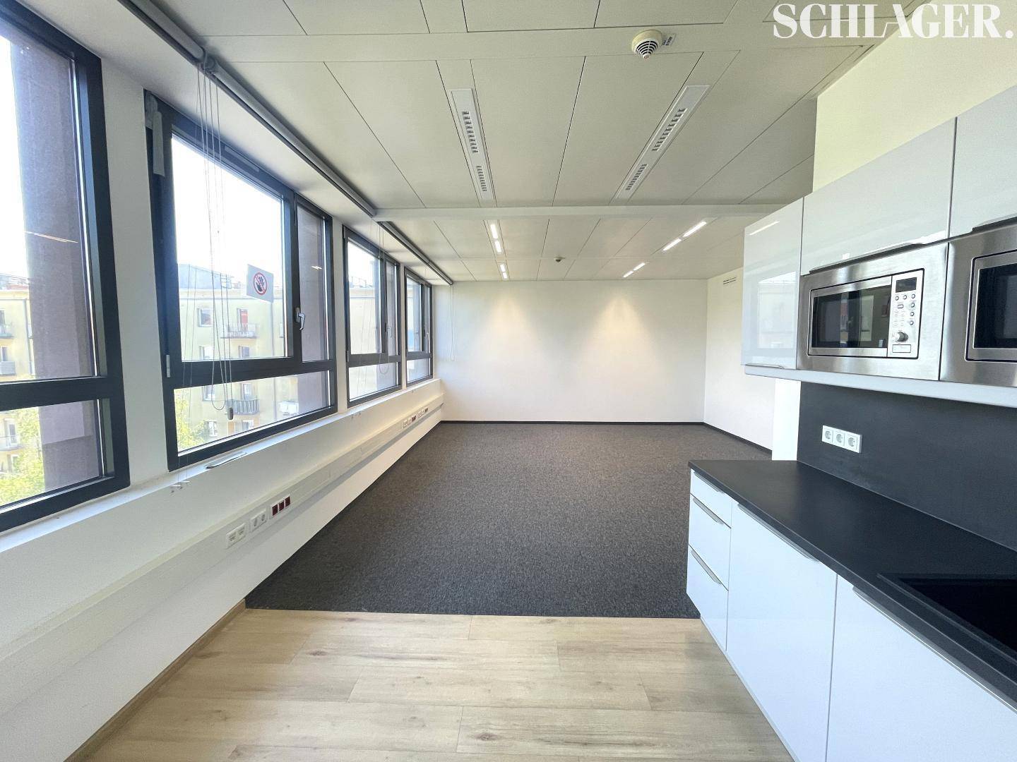 Kleine, moderne Küchenzeile in einem Büroraum mit hellen Holzfußböden und großen Fenstern.