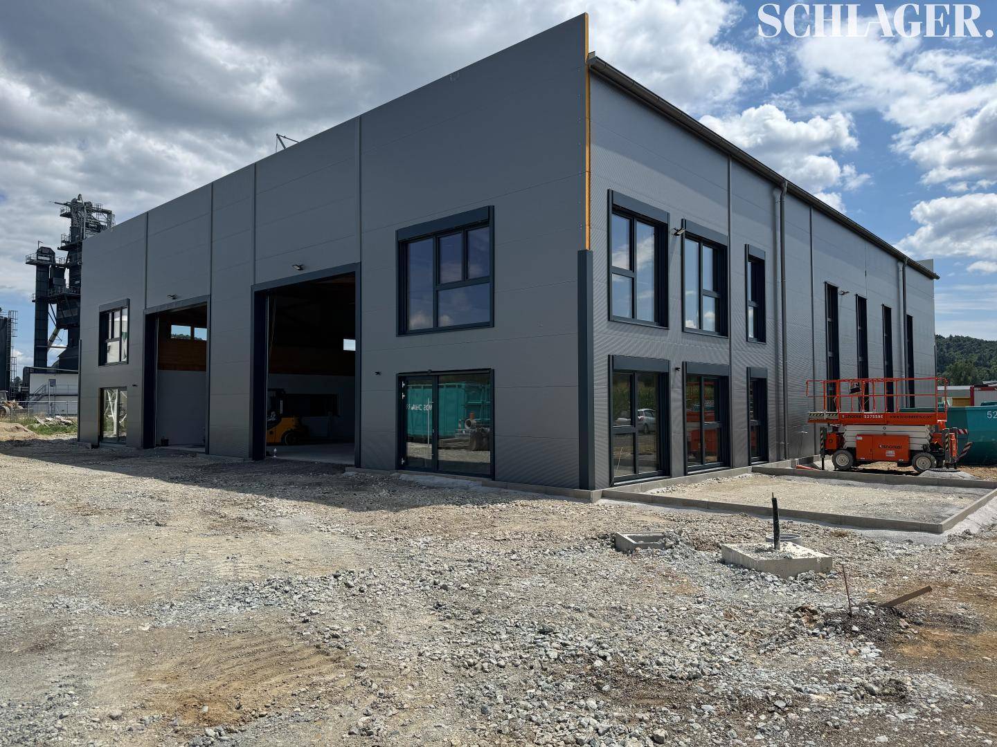 Außenansicht eines modernen Gewerbegebäudes im Bau mit grauer Fassade und großen Fensteröffnungen.