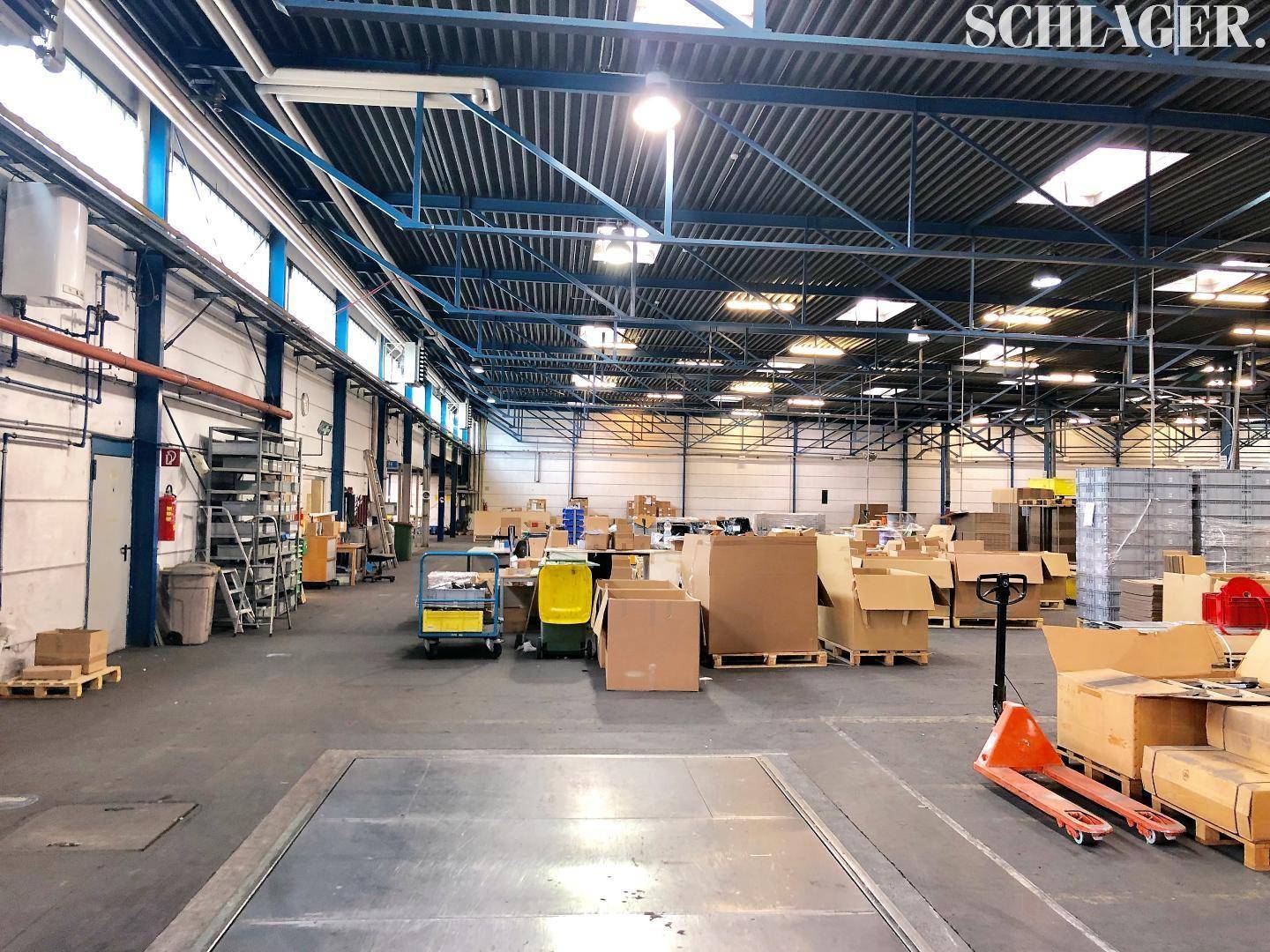 Weitläufige Lagerfläche mit hohen Decken, großen Fenstern und industrieller Beleuchtung.