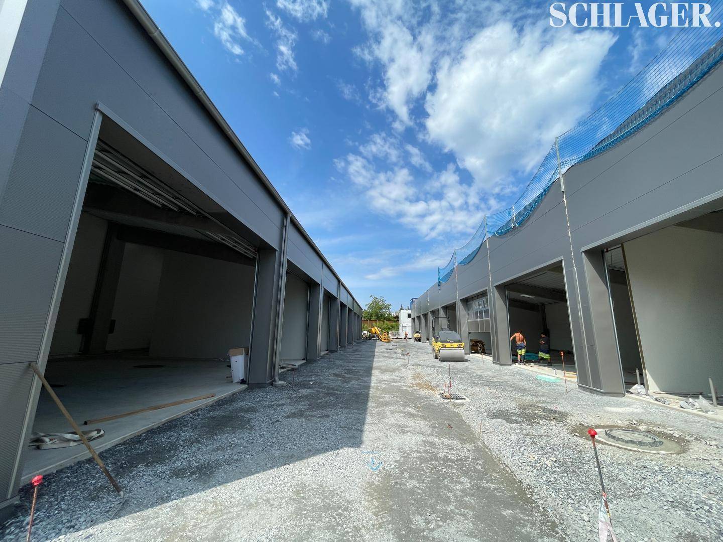 Reihe von neuen Gewerbeeinheiten mit großen Einfahrtstoren auf einer Baustelle bei sonnigem Wetter.