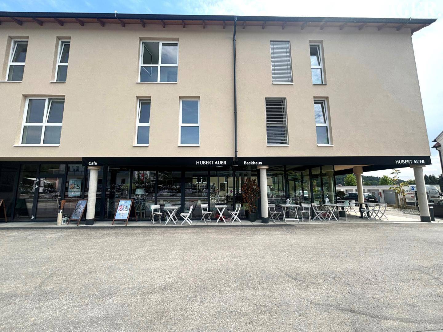 Frontansicht des modernen Geschäftsgebäudes mit Café, Bäckerei und Außenbereich unter einem Vordach.