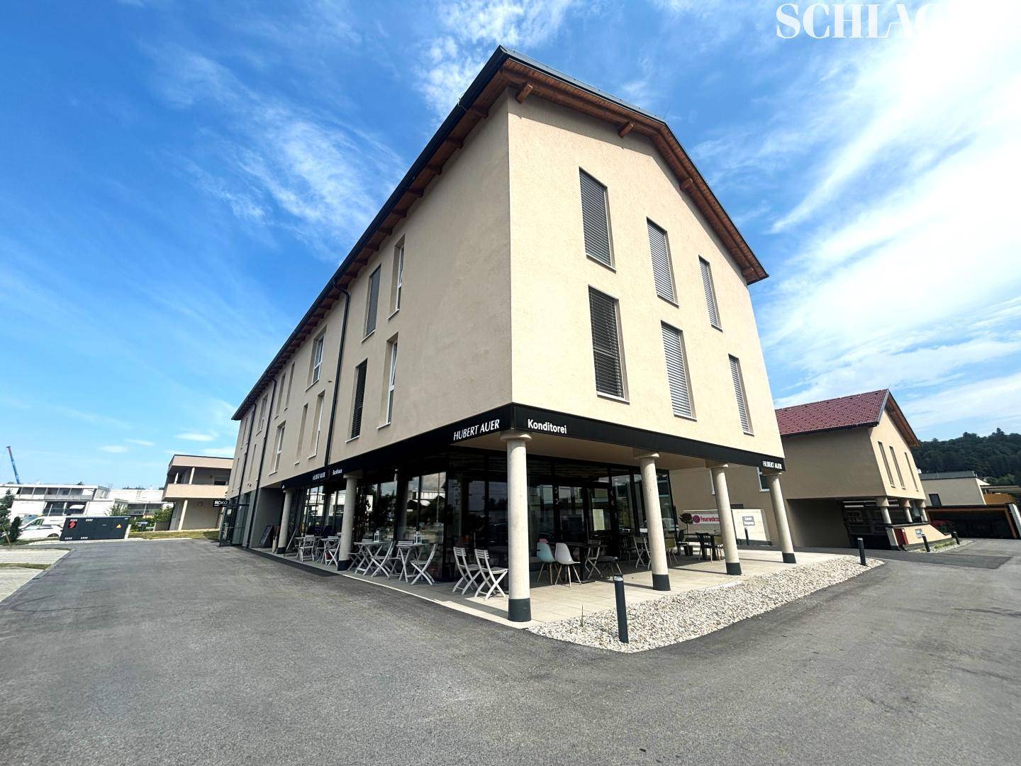 Modernes Geschäftsgebäude mit Café im Erdgeschoss und Wohnungen darüber unter blauem Himmel.