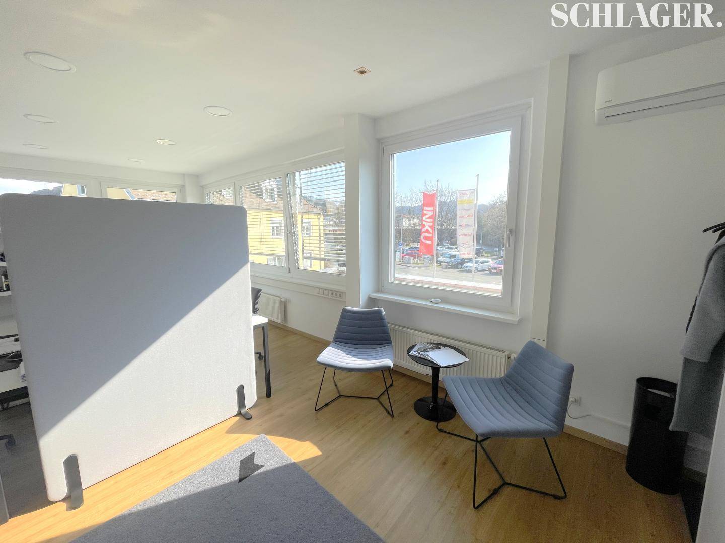 Heller Wartebereich oder Lounge im Büro mit modernen Stühlen, einem Raumteiler und großen Fenstern.