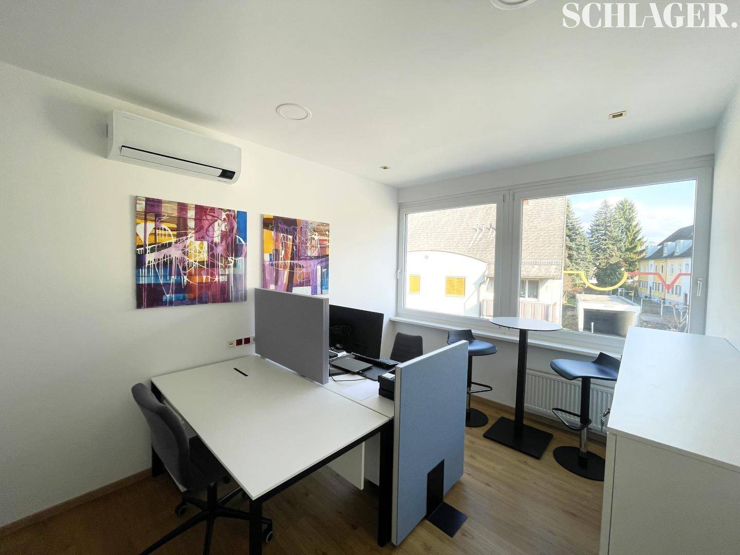 Helles Büro mit zwei Arbeitsplätzen, modernen Kunstwerken, Klimaanlage und Blick ins Grüne durch große Fenster.