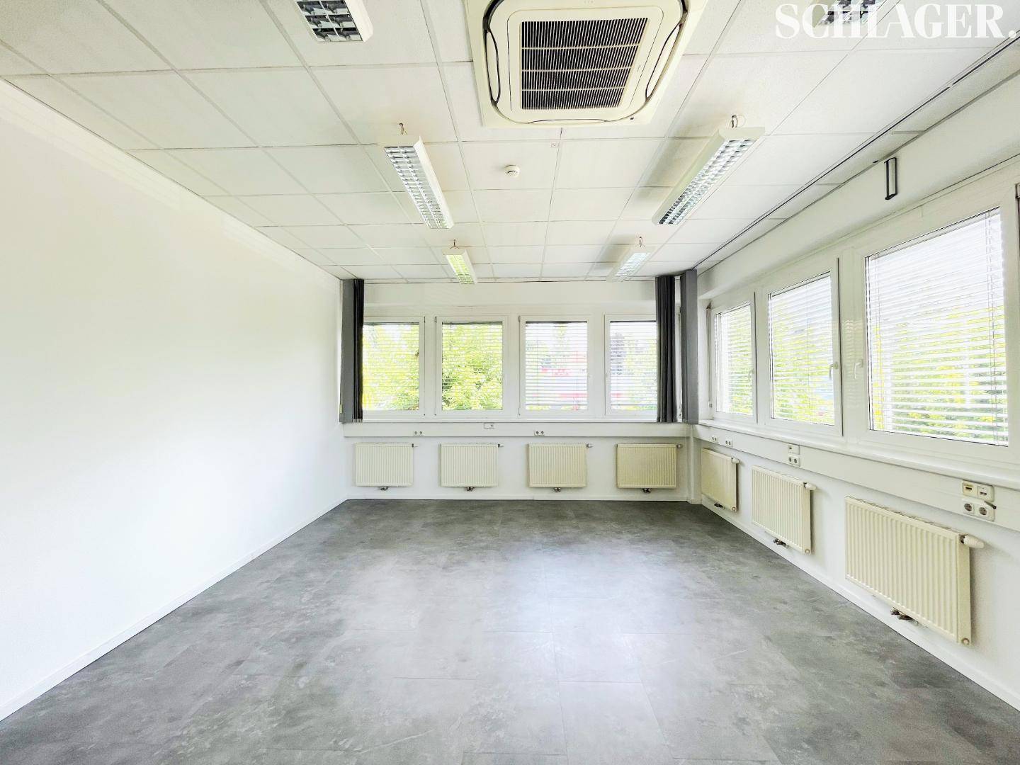 Helles Eckbüro mit vielen Fenstern an zwei Wänden, Klimaanlage und abgehängter Decke.