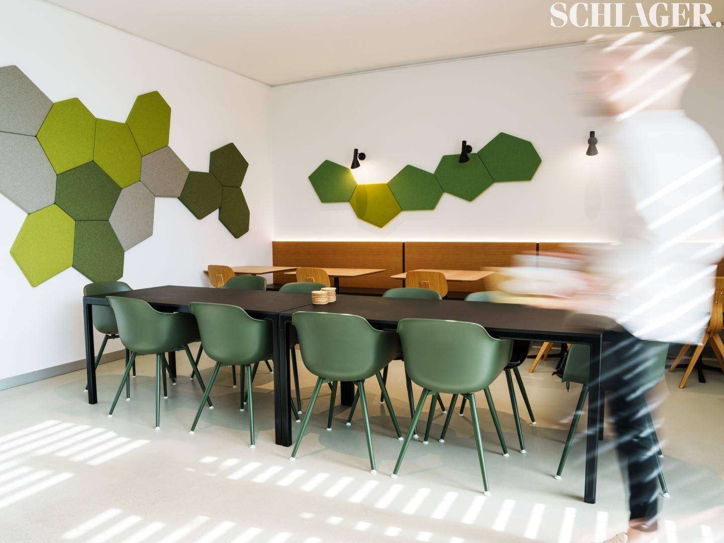 Moderner Pausenraum mit grünen Stühlen, Holztischen und dekorativen Akustikpaneelen an der Wand.